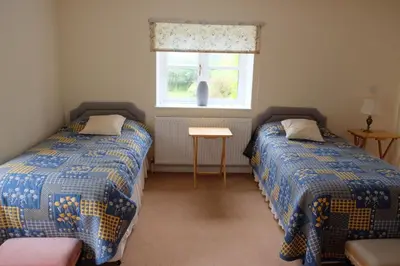 two beds in a room with a window and a table at Okewoon Barn in Lanivet