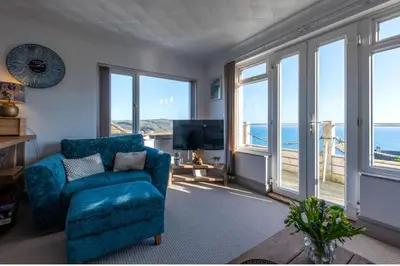 a living room with a blue chair and large windows at 1 Bed Flat - Sleeps 2 - Pets - Balcony - Parking in Looe