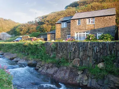 a house with a stone wall next to a river at The Old Store House in Boscastle