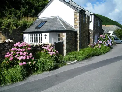 a small house with pink flowers in front of it at The Old Store House in Boscastle
