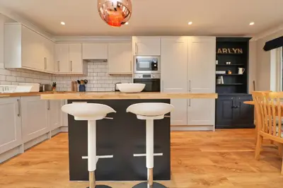 a kitchen with white cabinets and a black island with stools at BY THE BEACH cottage, dogs welcome in St Merryn