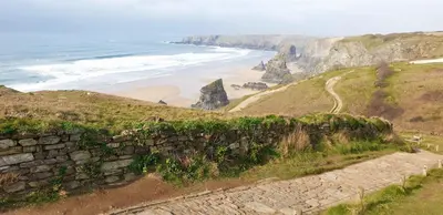 a stone wall next to a beach and the ocean at The Duchy Barn at Tregoose Old Mill in Newquay