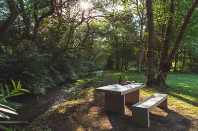 a picnic table and bench in a park with trees at The Duchy Barn at Tregoose Old Mill in Newquay