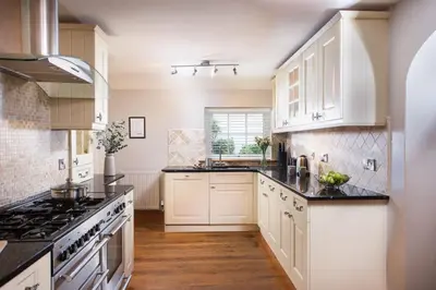 a kitchen with white cabinets and black counter tops at 3 The Manor - Opposite a golf course - Pet friendly - Wi-Fi in Uny Lelant