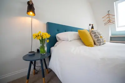 a bedroom with a bed with a blue headboard and a table with yellow flowers at The Coffee Loft in Padstow