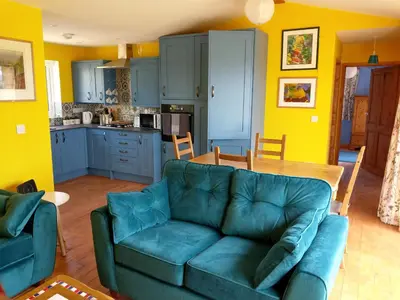 a living room with a couch and a kitchen at Orchard Chalet in Liskeard