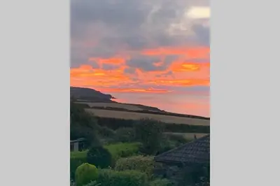 a sunset over a field with a house in the foreground at Trevone Luxury Shepherds hut close to the beach in St Merryn