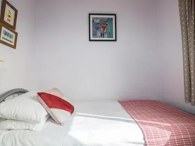 a white bed with a red and white pillow at Hazel Cottage in Tintagel