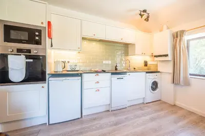 a kitchen with white cabinets and a washer and dryer at Polrunny Farm Elderberry Cottage with sea view in Boscastle