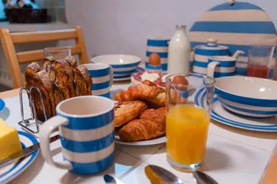 a table with a plate of pastries and cups of orange juice at Polrunny Farm Elderberry Cottage with sea view in Boscastle