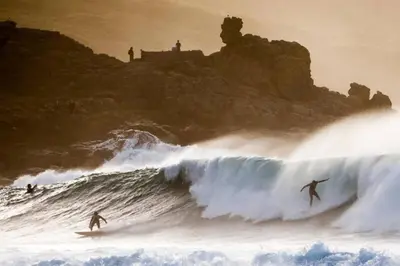 two surfers riding a large wave in the ocean at Driftwood Cottage in Uny Lelant