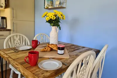 a wooden table with plates and a vase with yellow flowers at Driftwood Cottage in Uny Lelant