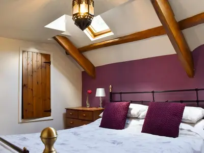 a bedroom with a bed with purple walls and wooden beams at Pineview Cottage in Downderry