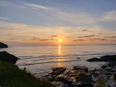 a sunset over the ocean with rocks in the water at Polrunny Farm Blackberry Cottage - Cornwall bliss in sight of the sea in Boscastle