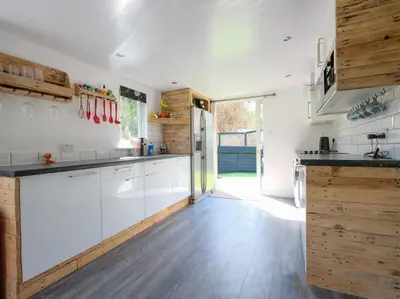 a kitchen with white cabinets and wooden floors at By The Beach in Torpoint