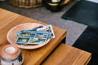 a wooden table with a plate with a magazine on it at Finest Retreats - Charnwood in Lewannick