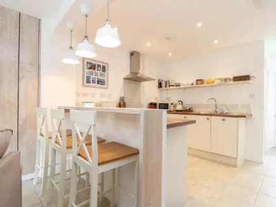 a kitchen with white cabinets and a kitchen island with stools at The Old Post Office in Helston