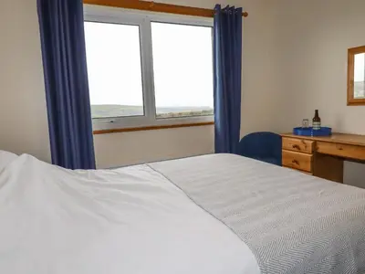 a bedroom with a bed and a desk and two windows at Boscastle View in Boscastle