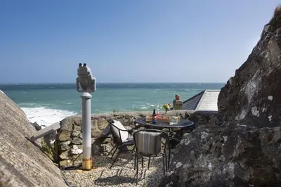 a table and chairs sitting on a rock near the ocean at Dolor Cottage in Coverack
