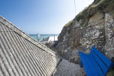a blue bench sitting on the rocks near the ocean at Dolor Cottage in Coverack