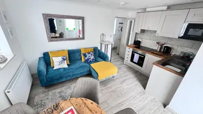 a living room with a blue couch and a kitchen at ABOVE PORTHMINSTER BEACH - 