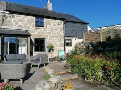 a stone house with two chairs and a patio at Trenwith Bridge Cottage in St Ives