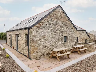 a stone cottage with two picnic tables on a patio at The Cornstore in Bodmin