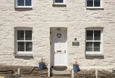 a stone building with a white door and two windows at Oriel Cottage in St. Agnes