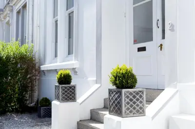 a white front door of a white house with two potted plants at Park View in Falmouth