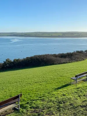 two benches sitting in a field overlooking a body of water at No 10 Treverbyn Road B & B in Padstow