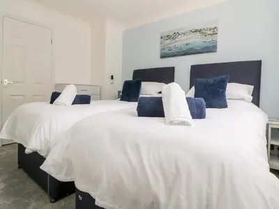 two beds in a room with white and blue pillows at Beach Cottage in Redruth