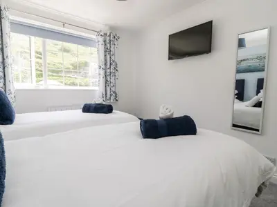 two white beds in a white bedroom with a tv at Beach Cottage in Redruth