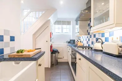 a kitchen with white cabinets and blue and white tiles at Stone's Throw in St Ives