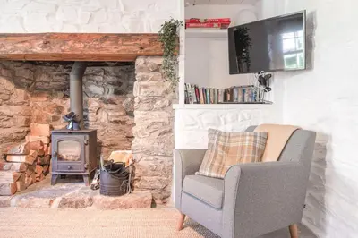 a living room with a chair and a stone fireplace at Salty's Cottage in St. Agnes