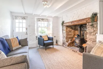 a living room with a stone fireplace and a chair at Salty's Cottage in St. Agnes