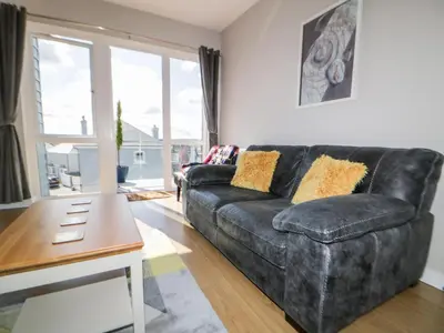 a living room with a black leather couch and a table at 23 Tre Lowen in Newquay