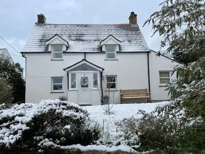 a white house with a bench in the snow at Rose Cottage Bee Happy anex in Newquay