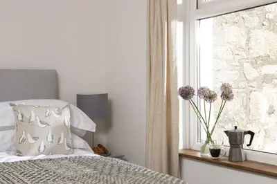 a bedroom with a bed and a window with flowers at Greenfields Coach House - Balcony with stunning ocean view in Marazion