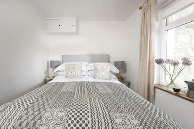 a white bedroom with a large bed with a window at Greenfields Coach House - Balcony with stunning ocean view in Marazion