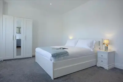 a white bedroom with a white bed and a night stand at Ocean View, Newquay - Free WiFi & Parking - Sea Views in Newquay