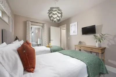 a bedroom with two beds and a television and a chandelier at Salt Life, Dunes at Upton Towans - Hot tub - Pet friendly - Self check in in Hayle