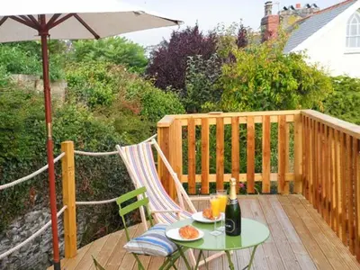 a table and chairs on a deck with an umbrella at Rose Cottage in St Austell