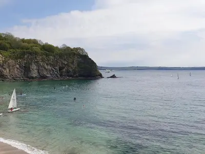 a sail boat in the water near a beach at Robin Hill in St Austell