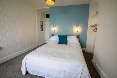 a bedroom with a large white bed with a blue wall at OA Surf Club in Bude