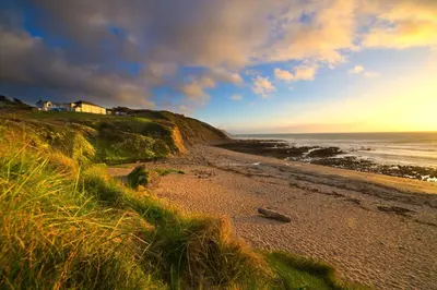 a beach with a house on a hill next to the ocean at OA Surf Club in Bude