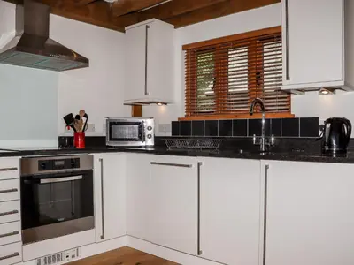a kitchen with white cabinets and black counter tops at Bybrook Lodge in Camelford