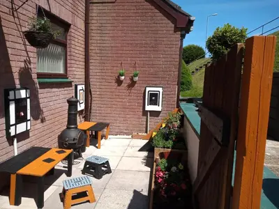 a patio with benches and a grill next to a brick building at West Looe Downs in Looe