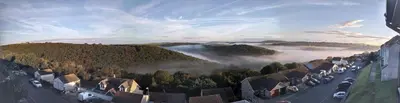 a town with cars parked on a road with fog in the hills at West Looe Downs in Looe