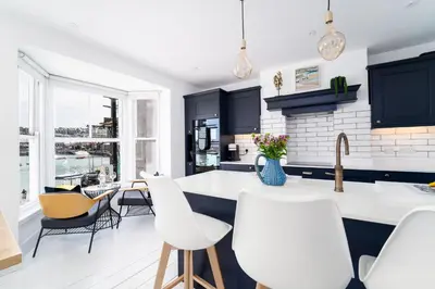 a kitchen with white and black cabinets and white chairs at St Ives House in St Ives