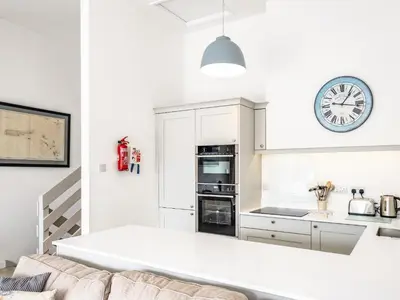 a kitchen with white cabinets and a clock on the wall at Slipway 10 in Padstow